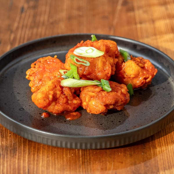 RaaSa Indian Cuisine's orange-glazed chicken pakora appetizer, garnished with fresh green onions on a dark plate.