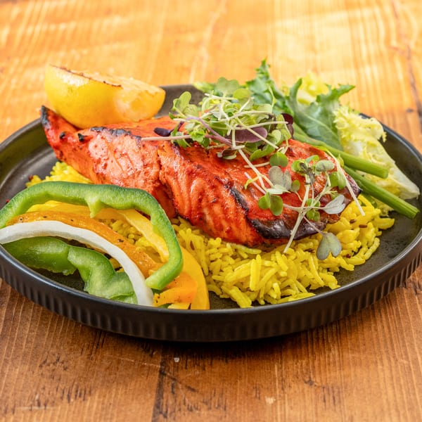 Indian salmon dish with yellow rice, bell peppers, and microgreens on a black plate.
