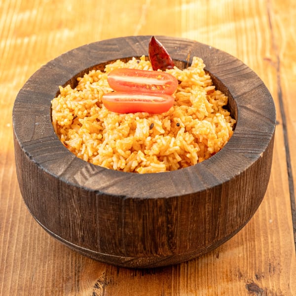 Indian tomato rice with spices, garnished with tomato slices and a red chili in a wooden bowl.