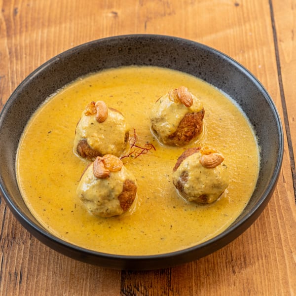 Four Indian malai kofta dumplings in a creamy yellow sauce, garnished with cashews and saffron.