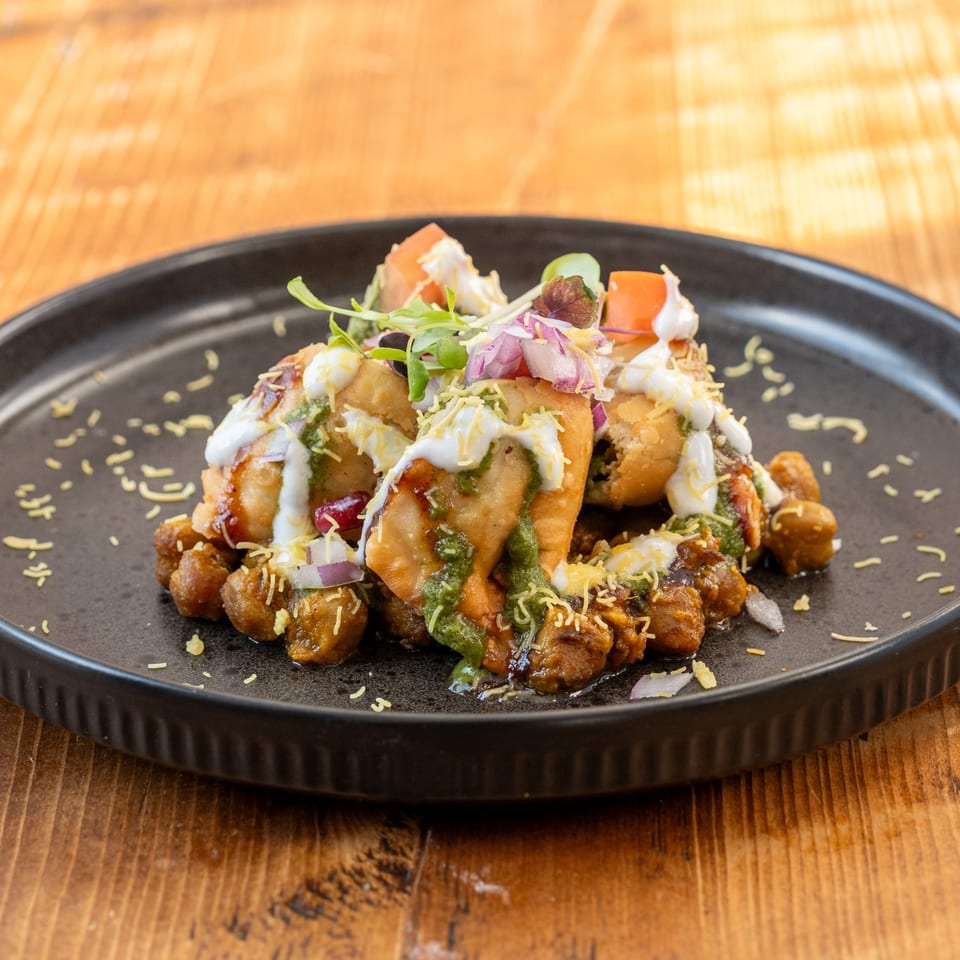 RaaSa Indian Cuisine's samosa chaat, topped with yogurt, green chutney, and fresh vegetables.