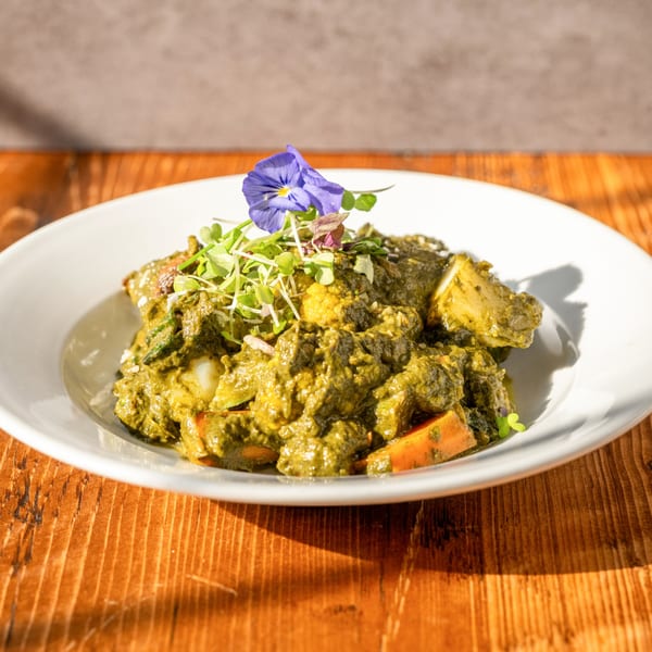 RaaSa Indian Cuisine's green curry with vegetables, garnished with microgreens and a purple edible flower.