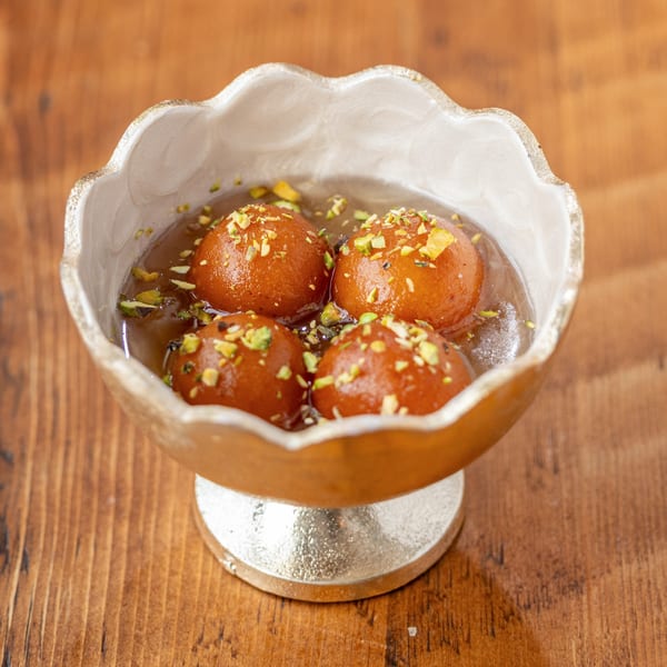 Four gulab jamun, Indian fried dough balls in syrup, garnished with pistachios in a decorative bowl.