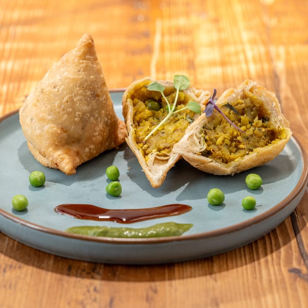 Two RaaSa Indian Cuisine samosas, one whole and one halved, with peas and sauces on a blue plate.